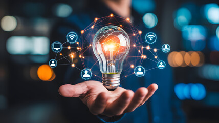 Hand holding a glowing light bulb surrounded by digital network icons representing innovation and connectivity in a modern city at night