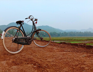 Fototapeta premium Vintage bicycle in rice field. Classic old road bike on rural dirt road with mountain background. Sustainable travel, country lifestyle, and World Bicycle Day 2026 concept in tropical landscape.