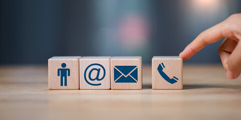 A hand touches wooden blocks with icons for user, email, phone, and contact, representing digital communication, customer support, contact us, and business connection solutions.