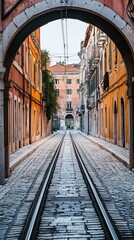 A narrow, paved street with train tracks, passing under an archway
