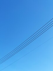 Fototapeta premium Minimalist composition of stark black power lines against a vibrant clear blue sky, creating a simple geometric abstract background with strong contrast.