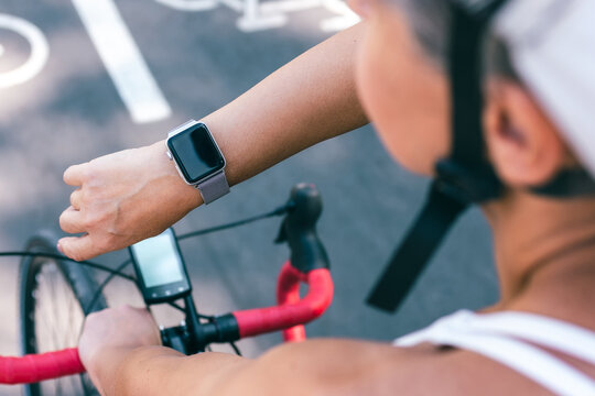 Close-up view of cyclist woman using smartwatch during outdoor ride on marked bike lane - Powered by Adobe
