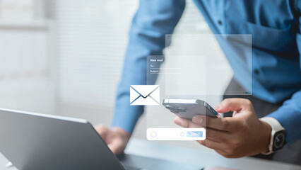 A business professional using smartphone and laptop to compose a new email, showing digital mail icons and interface elements, representing modern communication and productivity.