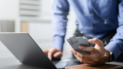 Business person using smartphone and laptop with chat icons, symbolizing live chat support, online customer service, and digital communication in a modern business environment.