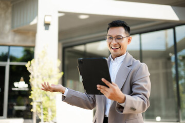 Happy businessman raising fist and cheering with smartphone in hand, celebrating success and victory with excitement and joy outdoors.
