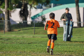 Obraz premium A 6 to 7 year old soccer player boy running on the field. Youth soccer.