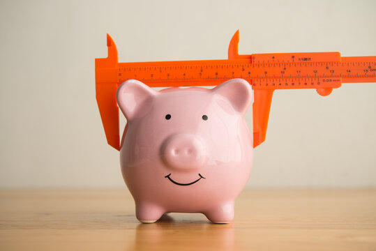 Measure size of piggy bank by vernier caliper on wooden table. Savings planning management and evaluation for achieve target, financial risk management, investment, money safety concept.