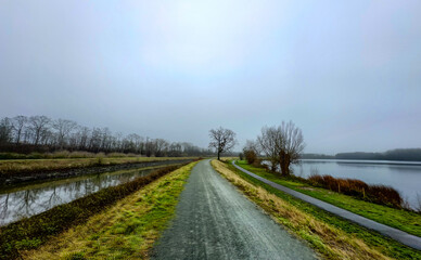 A serene and peaceful path runs beside a calm river, beautifully surrounded by lush nature on a...