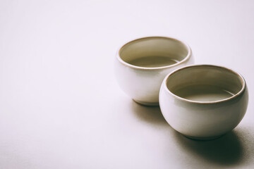 Two white ceramic cups sit slightly apart on clean white table, minimalistic style, soft natural light, calm and peaceful atmosphere, empty drinkware, simple design