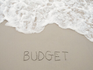 Fototapeta premium BUDGET handwritten with ocean waves on a sandy beach. The concept about budget planning and allocation