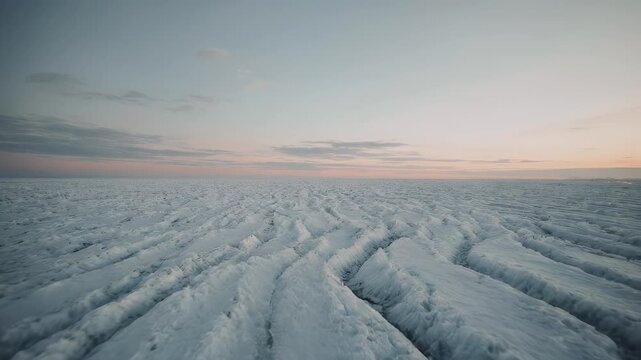 Frozen, cracked ice field stretches to the horizon under a pale, subtly colored sky at dusk or dawn