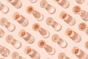 Top view glasses of rose wine on peach color background, beautiful shadows at sun. Vintage modern wineglass minimal life style, close-up sparkling alcohol drink, summer holiday mood, festive setting