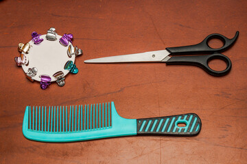 Scissors, comb, mirror, and colorful hair clips arranged on reddish surface, showcasing personal grooming tools in a playful and organized beauty setup.