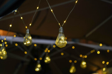 String of yellow lights hanging from a wire in the dark. The lights are evenly spaced and glow brightly, creating a warm and inviting atmosphere.