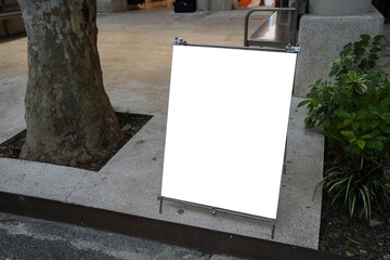 Blank white outdoor advertising stand or sandwich board mock up template. Clear street signage board placed by an outdoor dinning area of a restaurant. Background texture of standee on street.