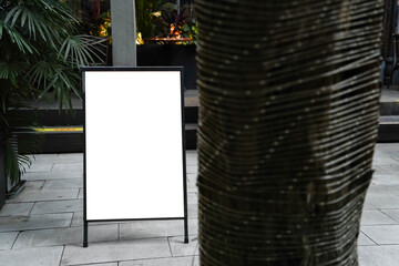 Blank white outdoor advertising stand or sandwich board mock up template. Clear street signage board placed by an outdoor dinning area of a restaurant. Background texture of standee on street.