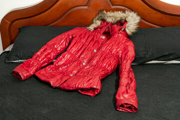 Red puffy winter jacket with fur-lined hood laid on black bedspread, showcasing insulated outerwear...