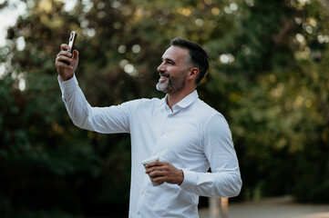 Smiling man making video call holding smartphone outdoors