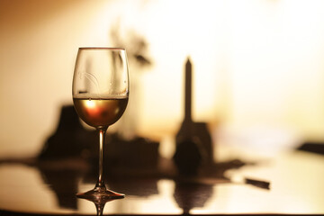 Shallow depth of field (selective focus) details with a glass of white wine on a table in a dark room with back light