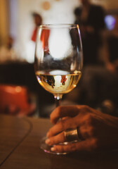 Shallow depth of field (selective focus) details with a glass of white in the hands of a woman at a party with people visible in glass.