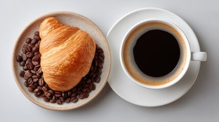 Delicious golden brown croissant rests on roasted coffee beans beside a white cup of black coffee on a clean white surface in overhead shot