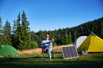Man using photovoltaic solar panel for charging portable power station outdoor in eco-friendly...