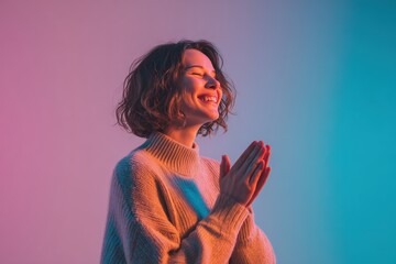 Joyful woman praying with serene expression in gradient lighting pink and blue background casual sweater spiritual mindfulness meditation inner peace gratitude positive emotions