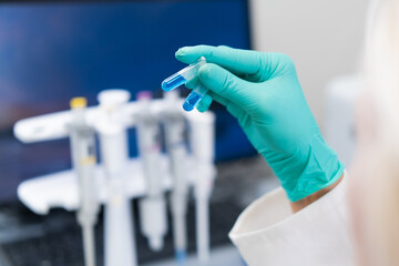 Female scientist in lab coat studying blue liquid in test tube used for DNA analysis and...