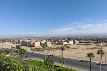 
مشهد بانورامي لحي سكني في ضواحي مدينة مغربية بشارع ونخيل تحت سماء صافية