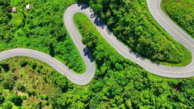 Drone aerial shot capturing a car navigating sharp turns on a high mountain road surrounded by dense jungle, reflecting danger, endurance, travel, discovery, challenge, and natural beauty. Thailand.
