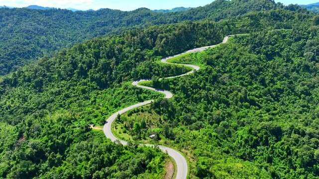 Stunning drone shot of a serpentine mountain road surrounded by lush greenery, representing risk, perseverance, connection, sustainability, travel, and the beauty of the natural world. Thailand.

