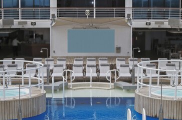 Guest pooldeck or swimmingpool with sun deck on modern family cruiseship or cruise ship liner with elegant lounge furniture deck chairs and rattan sun beds loungers