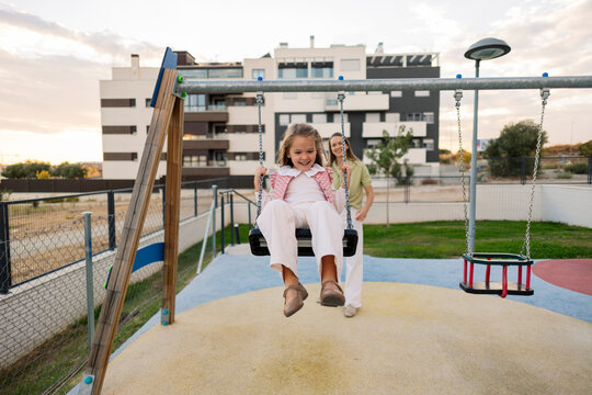 Mother pushing daughter on swing, enjoying playtime - Powered by Adobe