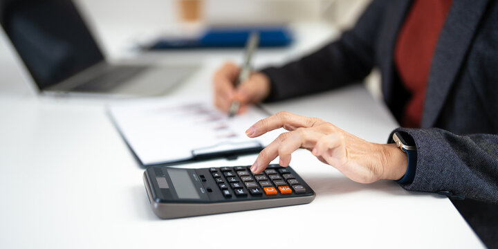 Close up of woman accountant using calculator to calculate tax refunds or  finance. woman doing finance with calculate expenses with laptop computer on office table.