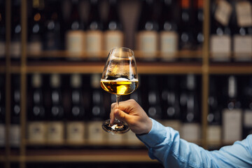 Expert Evaluating White Wine Glass Against Blurred Wine Cellar Background