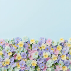 Obraz premium A delicate border of pastel pansies in pink, purple, yellow, and mint against a soft blue background, perfect for spring designs and greeting cards.