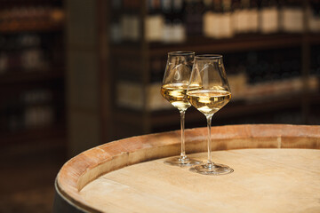 Two Glasses of White Wine Resting on Wooden Barrel in Wine Cellar