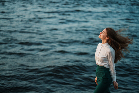 A woman in profile gracefully walks by a vibrant seascape, her hair flowing in the breeze, exuding a sense of tranquility and freedom.