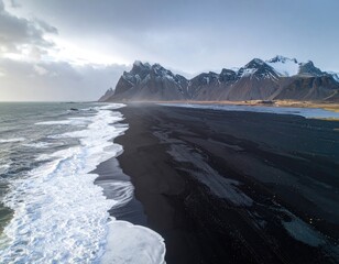 Obraz premium Dramatic black sand beach meets stormy waves, snow-capped mountains loom in the distance