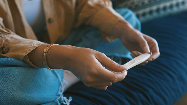 Pregnancy test, hands of woman and couch with check, maternity or hope in fertility outcome. Health, waiting and female person in home with medical stick, IVF and motherhood kit expectations.