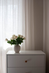 Vase with white roses on dresser table in bedroom. Interior element