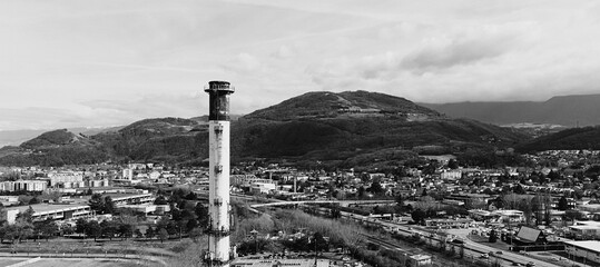 Monochrome industrial chimney with town and hills in background