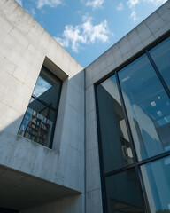 Obraz premium Modern concrete building with large glass windows and minimalist design, viewed from below against a blue sky, blending architecture with natural light and interior detail.
