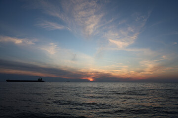 Dramatic sunset over the ocean with a cargo ship silhouette, scenic seascape with colorful clouds and sunlight, tranquil marine scene at dusk, nature background
