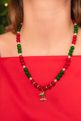 Close up on a girl wearing a satin dress and beaded necklace with a Christmas bell pendant next to the Christmas tree.
