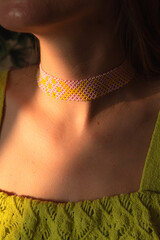A girl wearing a green dress and yellow and pink ethnic beaded necklace, close up on the handmade necklace.