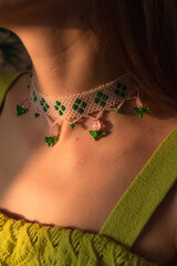A girl wearing a green dress and green and pink floral beaded necklace, close up on the handmade necklace.