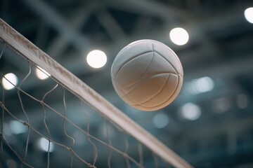 Closeup view of a white leather volleyball in motion near the net inside a gymnasium during a competitive match