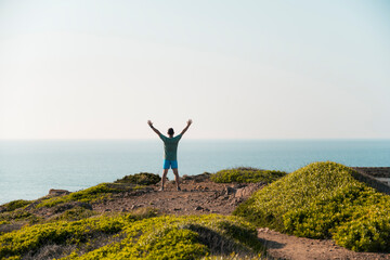 Man standing with arms raised facing the ocean horizon