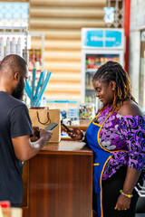 Mobile money cashless digital payment, African businesswoman assists a customer with mobile money transaction in her supermarket